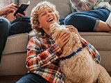 Una familia feliz sentada en la sala de estar. Su hijo está sentado en el piso con el perro de la familia lamiéndole la cara.