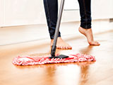 Image of a barefoot woman sweeping the floor with a dry mop.