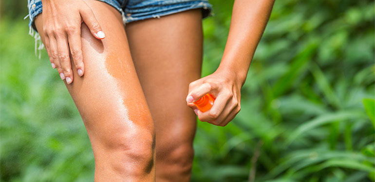 Woman spraying insect repellent on her legs outdoor in a nature forest.