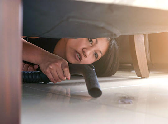 A woman bent down vacuuming underneath her sofa.