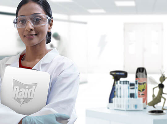 A smiling entomologist, wearing a lab coat and glasses, standing in a lab of the SC Johnson® Institute of Insect Science for Family Health