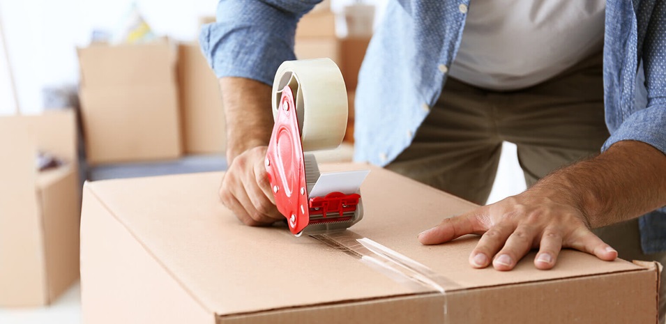 A man sealing a cardboard box with tape.