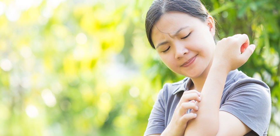 A young woman scratching her arm outside from a mosquito bite.